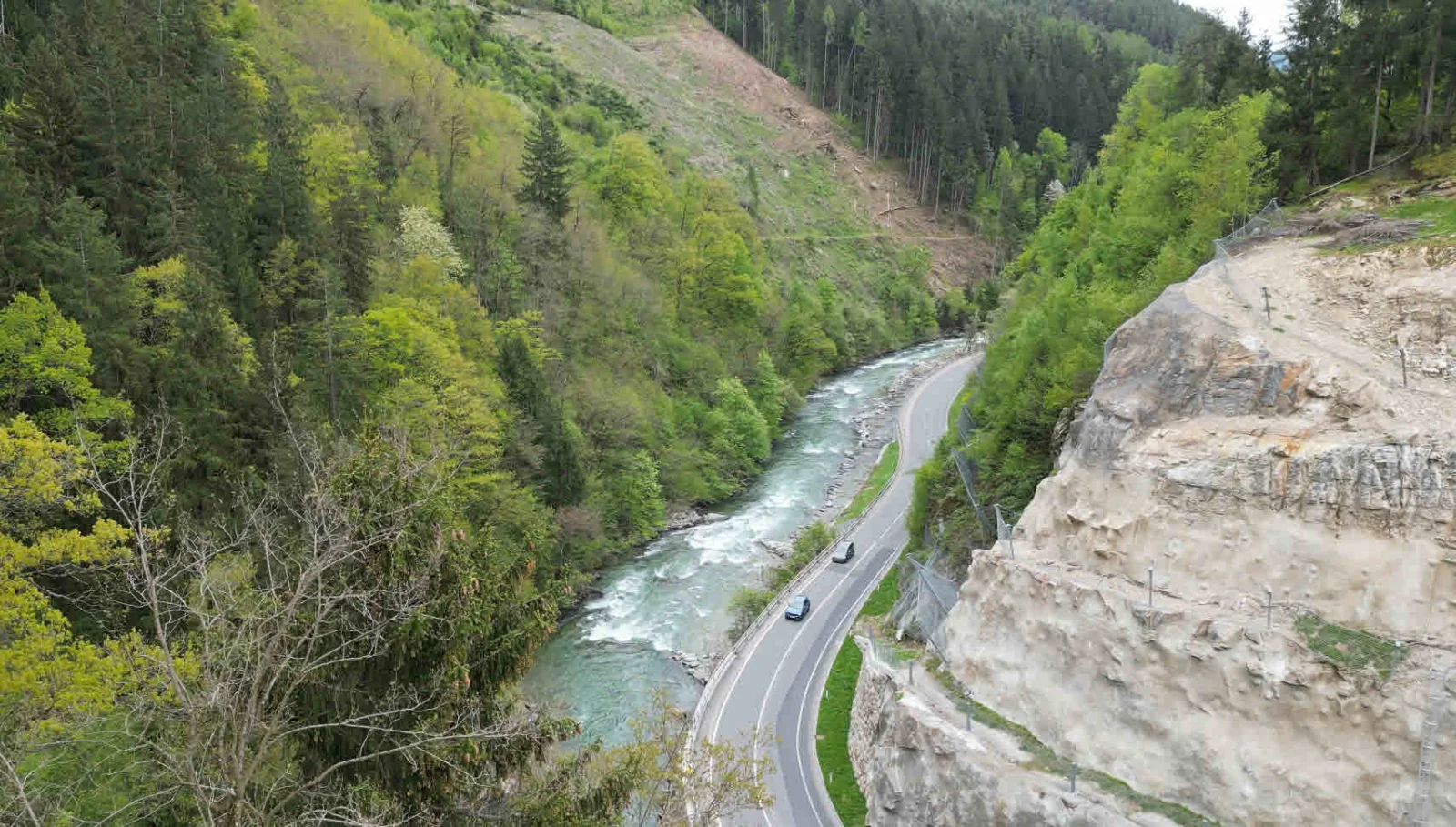 Bergstraße mit Fluss und bewaldeten Hängen in den Alpen