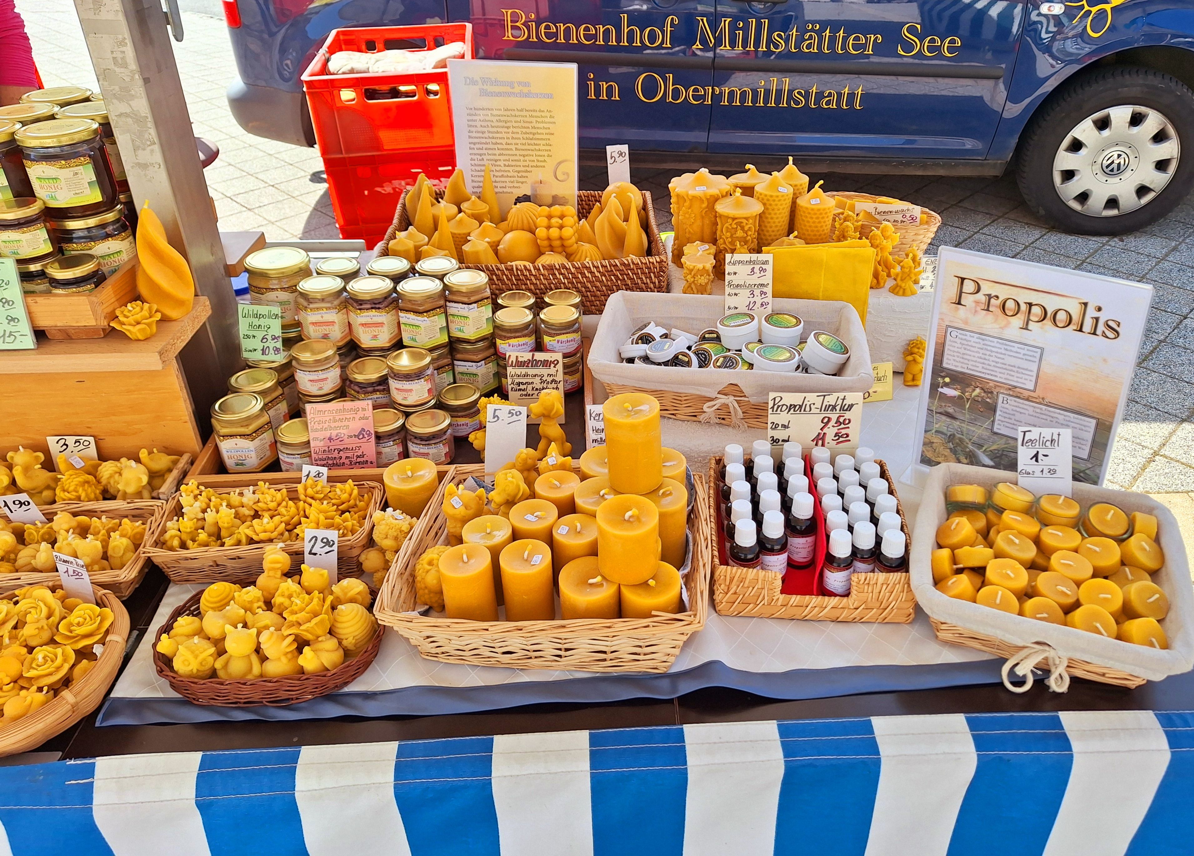 Das Bild zeigt einen Marktstand mit vielen verschienen Bienenwachskerzen die selbst hergestellt wurden. Zusätzlich noch Propolis und Honiggläser zum Kauf.